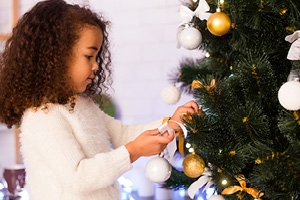 Little African American girl decorating Christmas tree at home