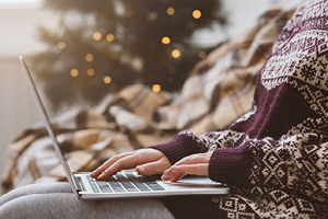 Woman in warm sweater using laptop over Christmas decorating room