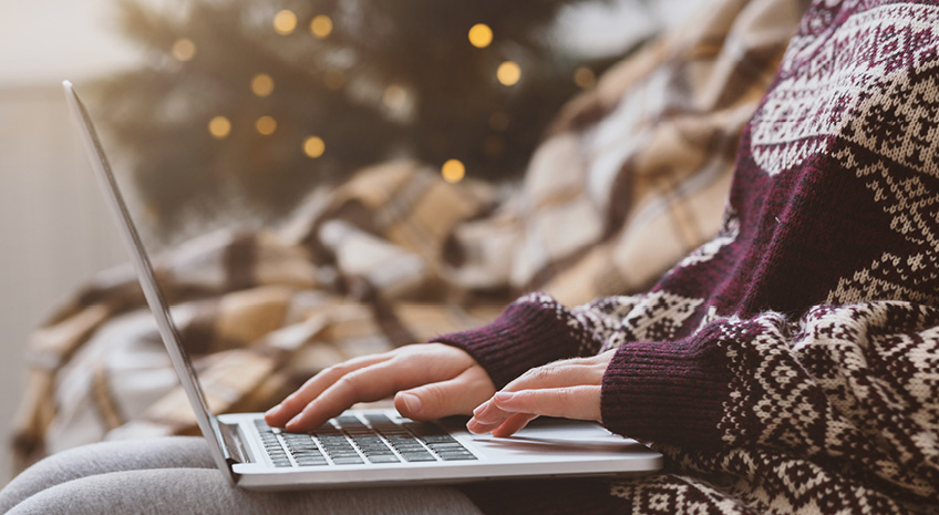 Woman in warm sweater using laptop over Christmas decorating room