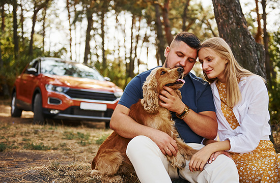 Couple with dog have weekend outdoors in the forest with car behind them.