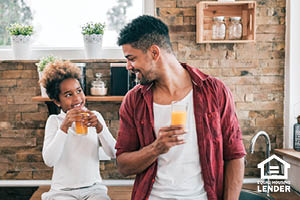 african american father and daughter sitting in kitchen drinking orange juice