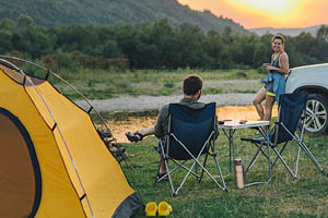 couple sitting in camp chairs looking at sunset above river in mountains
