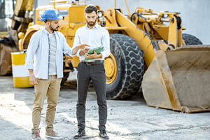 Builder choosing heavy machinery for construction with a sales consultant, signing some documents on the open ground of a shop with special vehicles