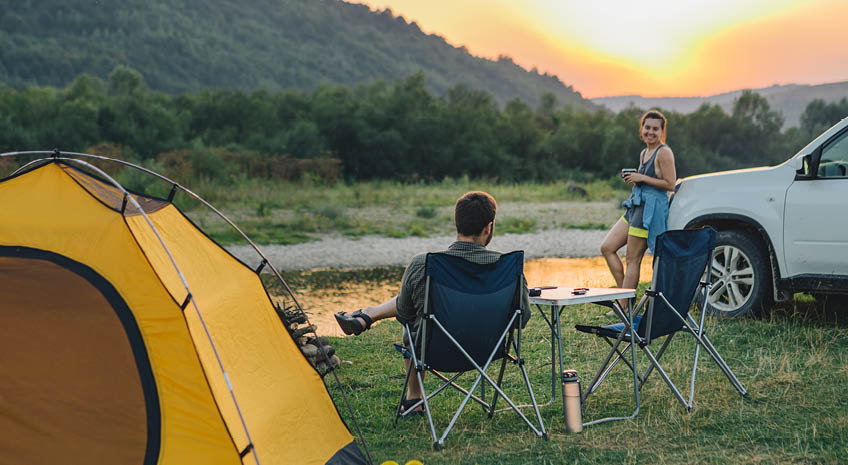 couple sitting in camp chairs looking at sunset above river in mountains