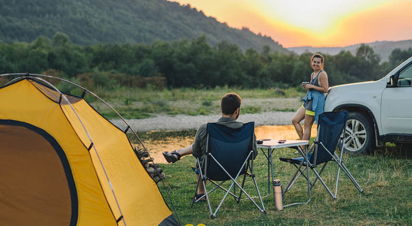 couple sitting in camp chairs looking at sunset above river in mountains