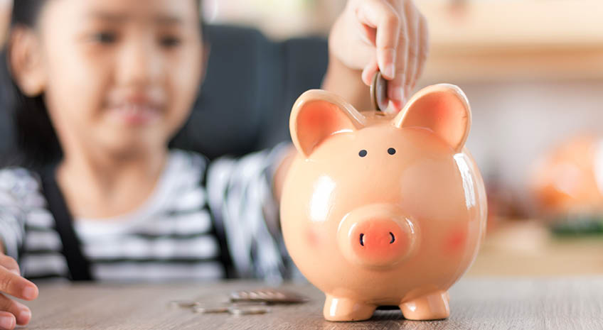 Asian little girl in putting coin in to piggy bank shallow depth of field select focus at the pig