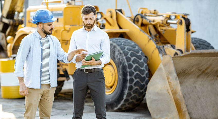 Builder choosing heavy machinery for construction with a sales consultant, signing some documents on the open ground of a shop with special vehicles