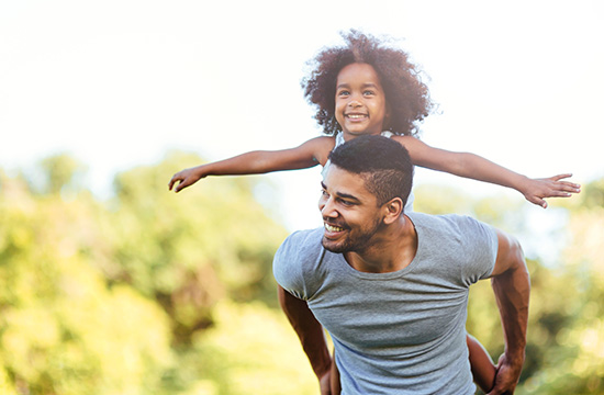Portrait of young father carrying his daughter on his back in nature