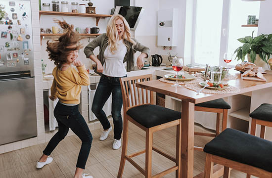 Full length portrait of charming blond woman spending time with her adorable kid. They dancing and laughing in kitchen