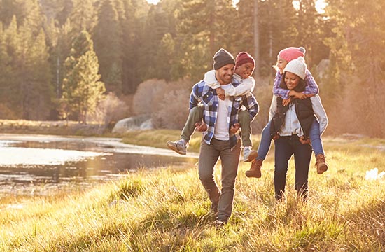 Parents Giving Children Piggyback Ride On Walk By Lake