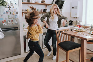 Full length portrait of charming blond woman spending time with her adorable kid. They dancing and laughing in kitchen
