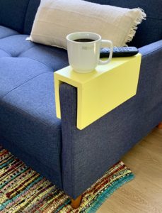 yellow wood arm rest on a blue couch with coffee cup on it