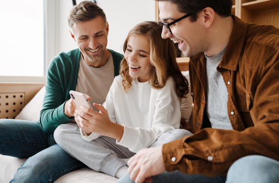 Happy family smiling and using mobile phone while sitting on couch