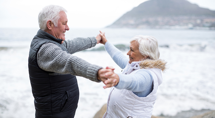 elderly couple standing together smiling on a beach