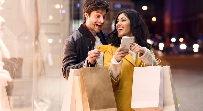 Consumerism concept. Happy couple checking cellphone outdoors