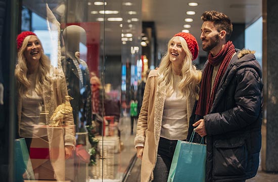 Front view of a couple walking past a shop window and looking in. They are shopping during the sales. The man is holding shopping bags.