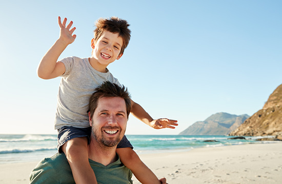 father holding son on his shoulders at the beach