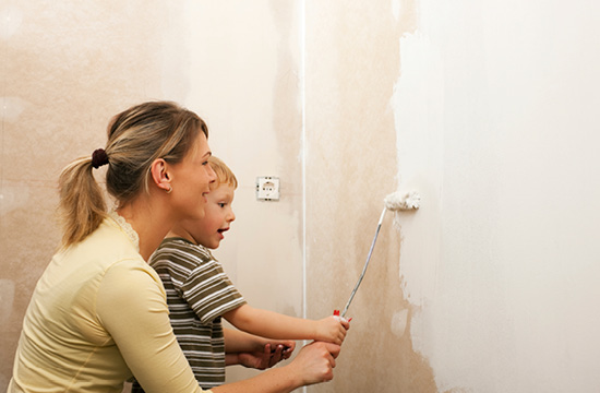 mother and young son holding paint roller and painting wall together
