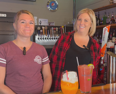 Dani and Kayla from Plymouth Pub in St Helens pose with 2 mixed drinks behind bar