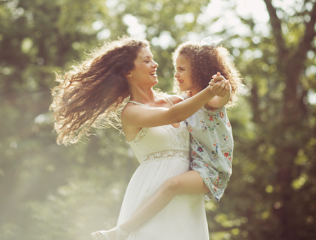 mother with long curly hair dancing at park with daughter in a dress