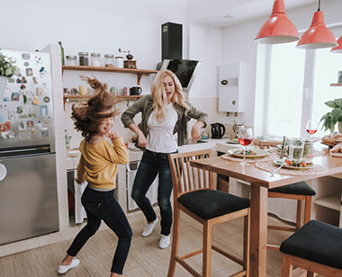 Full length portrait of charming blond woman spending time with her adorable kid. They dancing and laughing in kitchen
