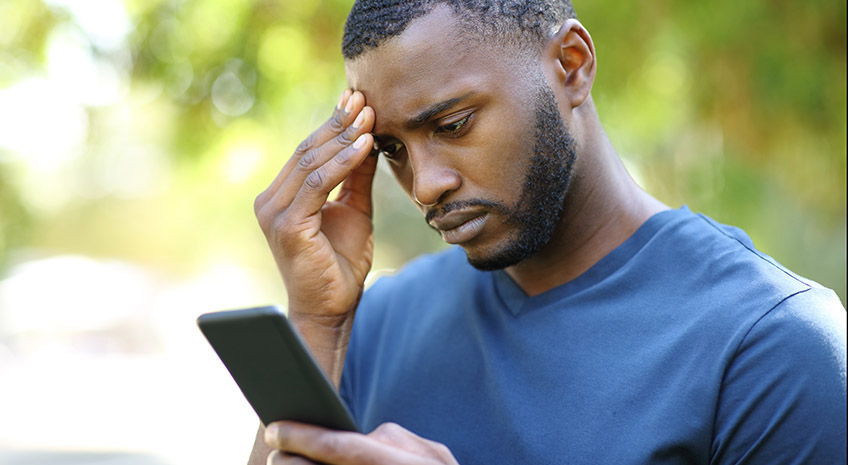 Worried black man checking smart phone in a park