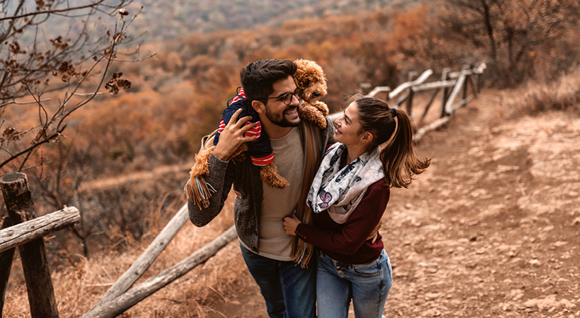 young hispanic couple hike together in the fall with their poodle.