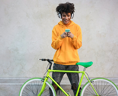African American male in yellow hoodie wearing headphones, on cell phone with green bike