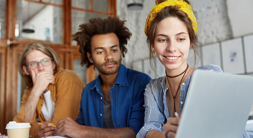 3 co-workers look on at a laptop during a meeting