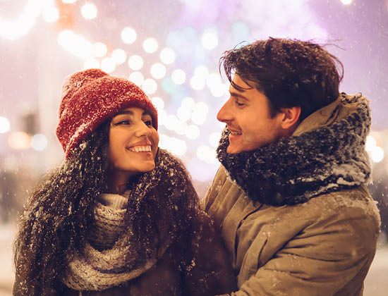 Latino man holding a woman. Dress in warm winter clothes. Dusted in snow.