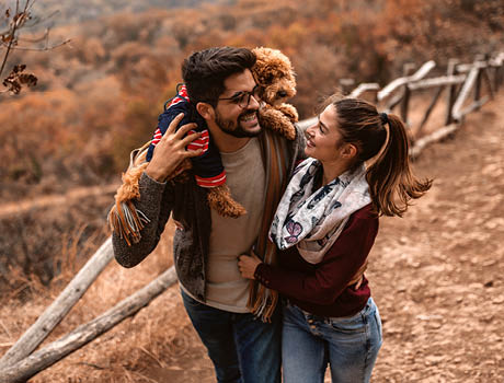 young hispanic couple hike together in the fall with their poodle.