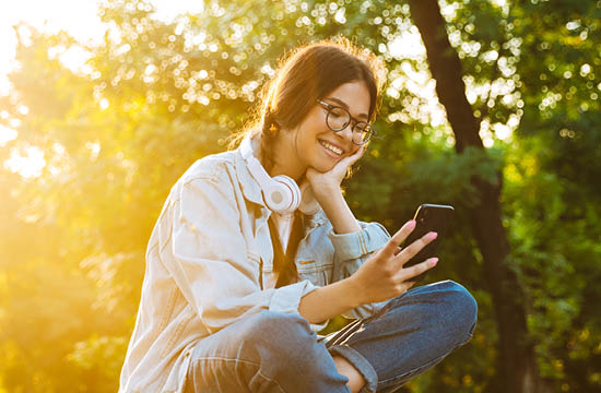 young bespectacled woman sitting cross legged while looking a phone
