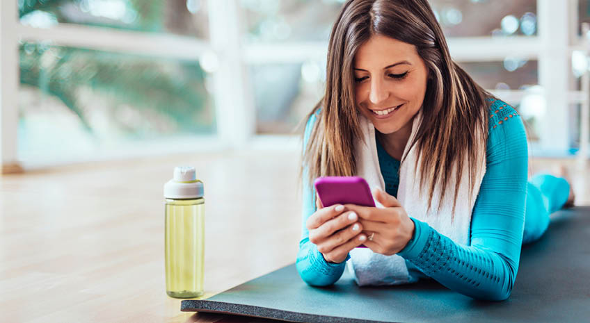 woman in blue laying on her stomach looking at phone after doing yoga class