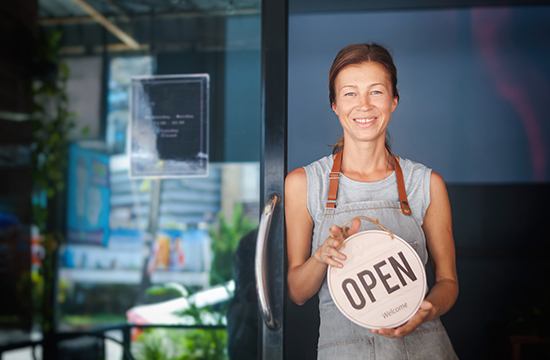 mature woman standing in doorway holding open sign