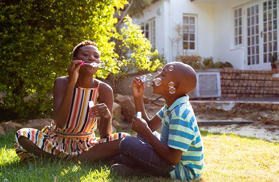 black mother and son sitting in front yard on a nice day blowing bubbles