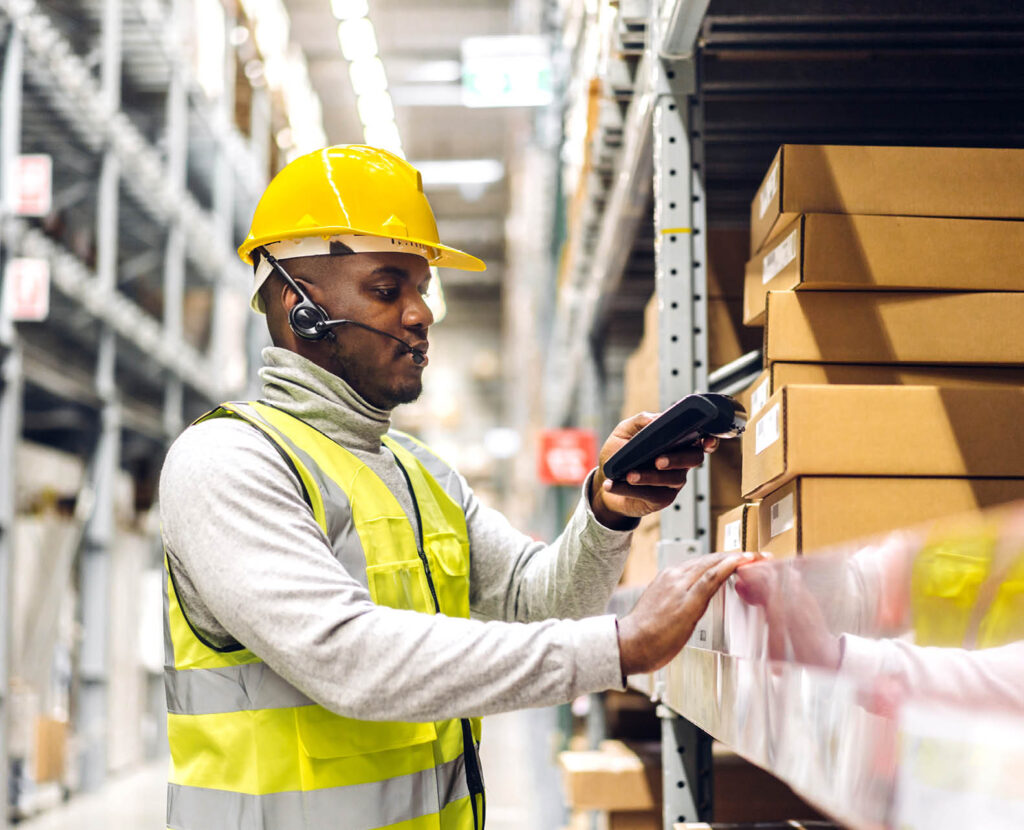 african american man in hard hat and reflective vest scanning boxes