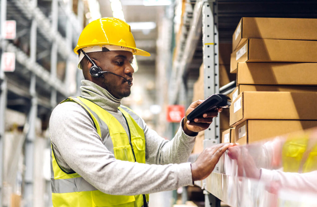 african american man in hard hat and reflective vest scanning boxes