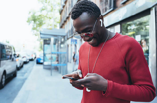 african american man in sunglasses and a red sweater looking at phone on the street.