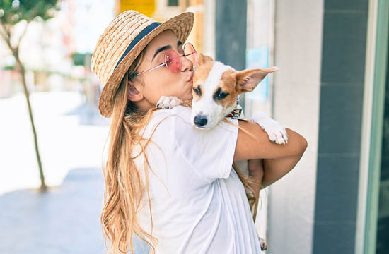 blonde Caucasian woman in white shirt nuzzling a dog on the sidewalk