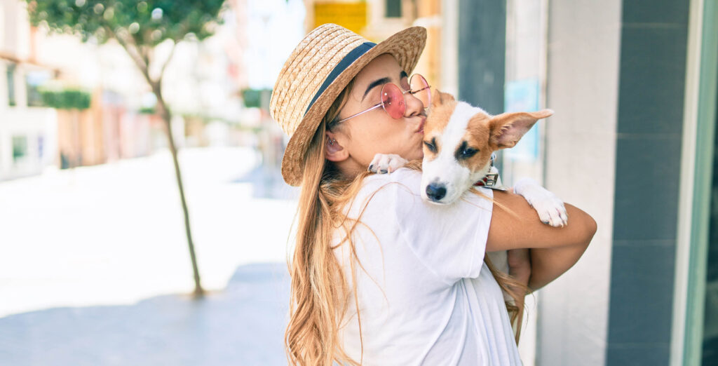 blonde Caucasian woman in white shirt nuzzling a dog on the sidewalk