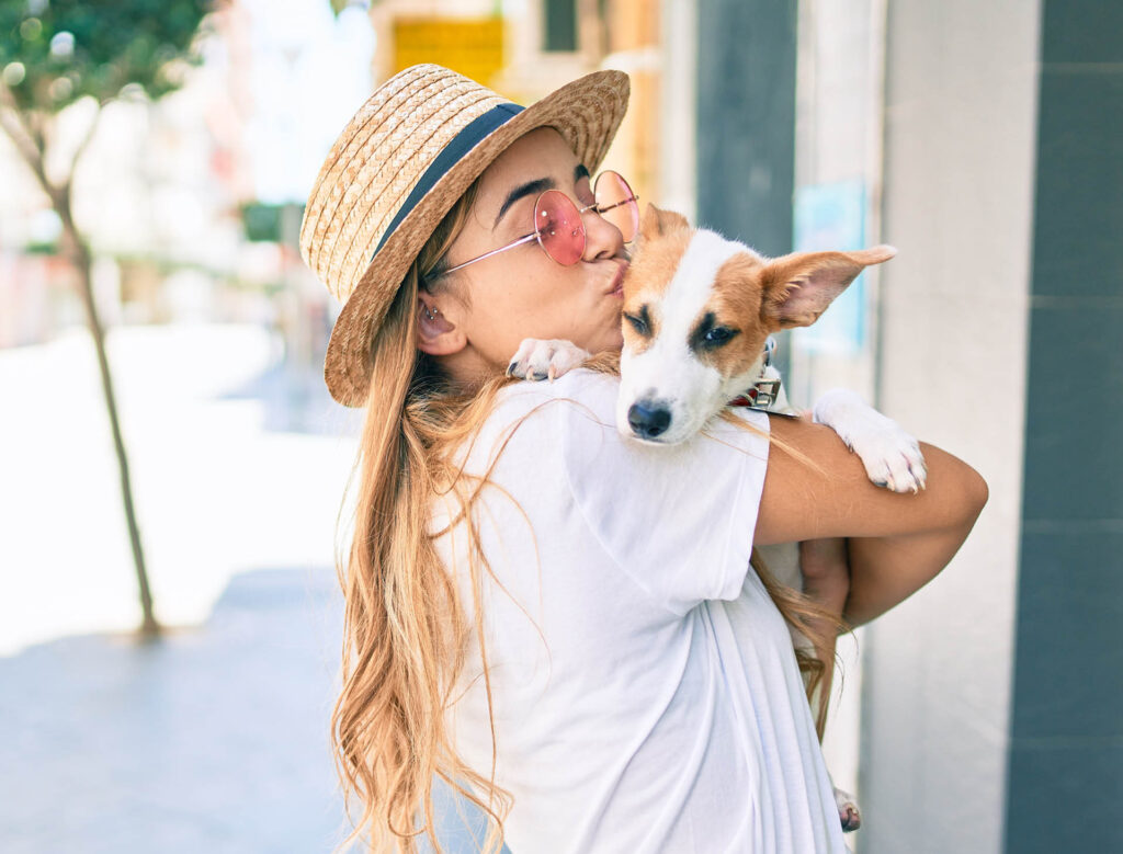 blonde Caucasian woman in white shirt nuzzling a dog on the sidewalk
