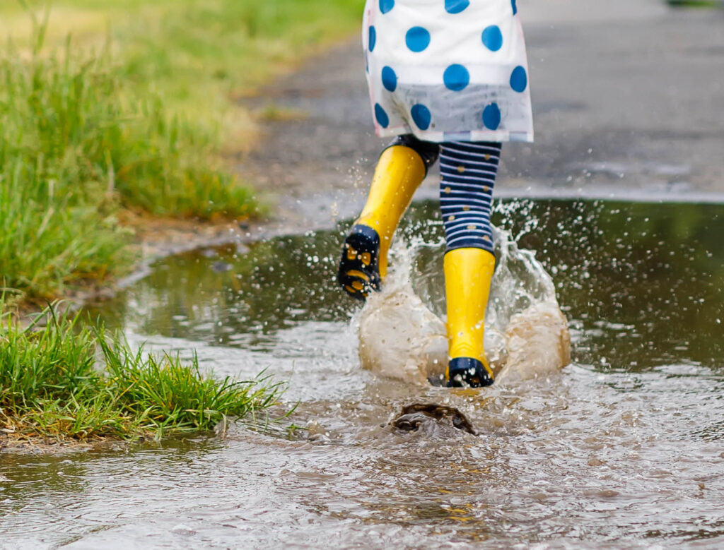 child in yellow rain boots a blue polka dot coat splashing in puddle