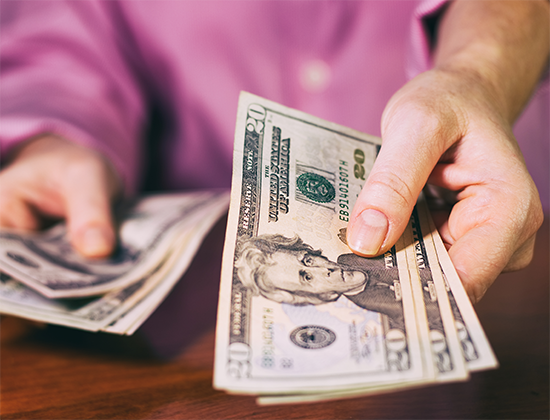 close up of hands holding cash out toward the viewer