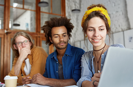 3 co-workers look on at a laptop during a meeting
