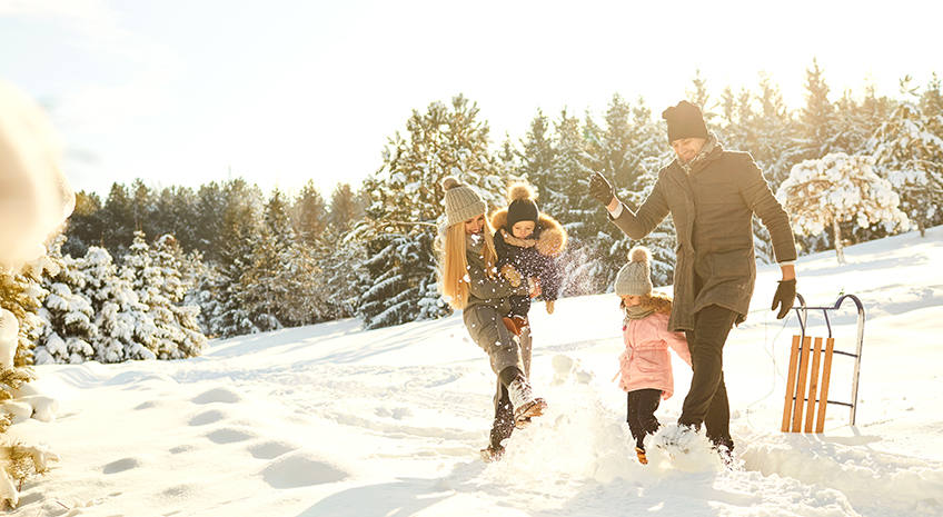family of 4 playing in snow, wearing winter clothing, and a bobsled