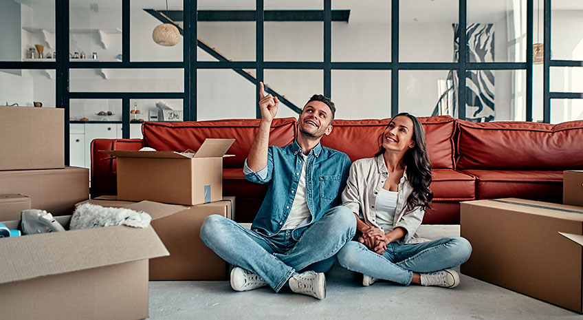 man and woman in new home, sitting on floor in front of couch with moving boxes