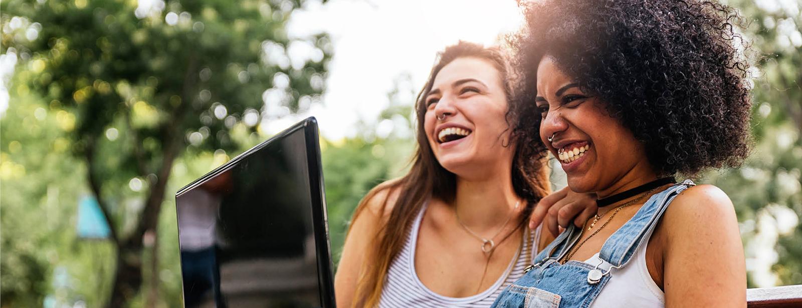 two women sitting on a bench with a laptop